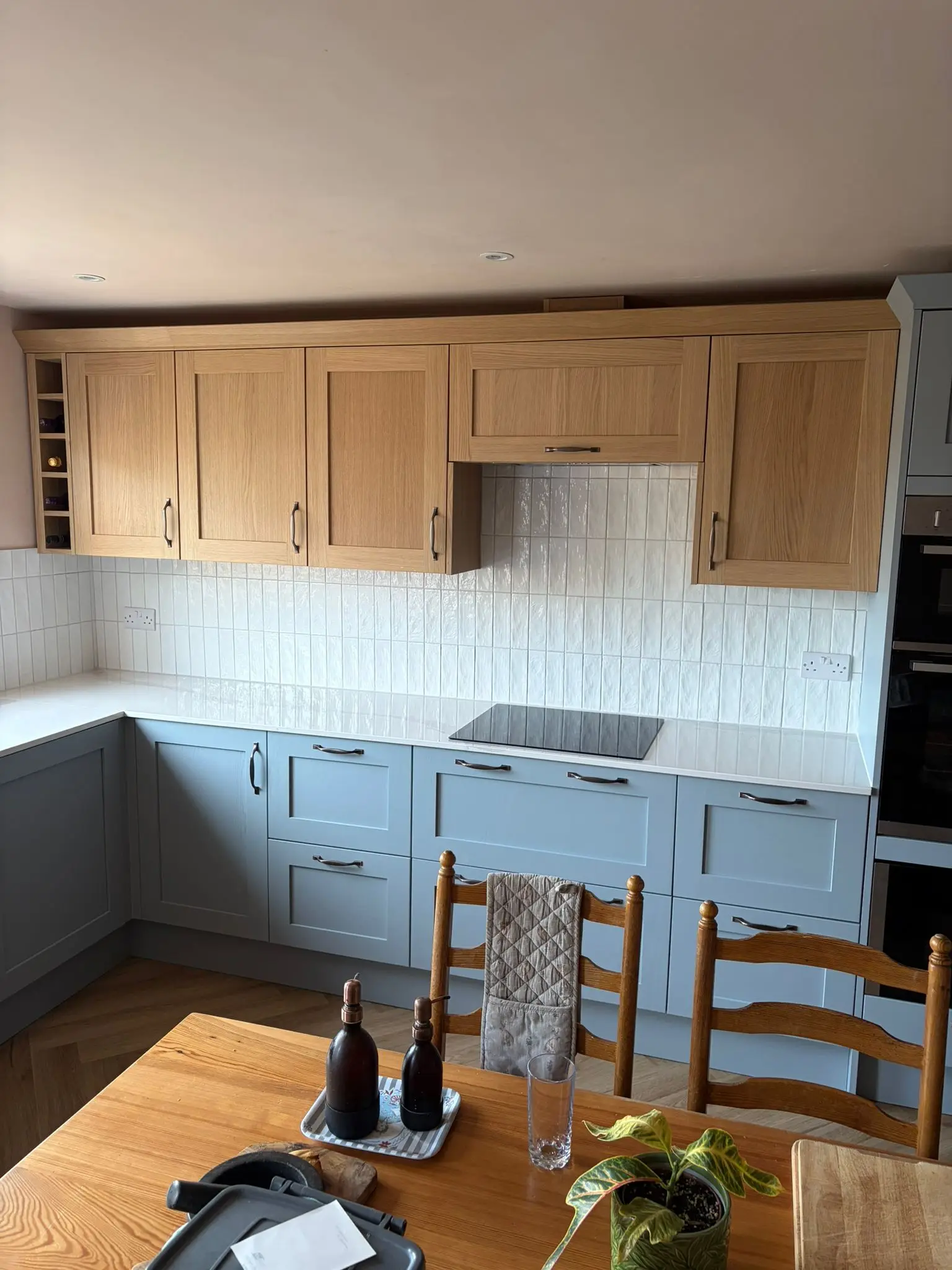 Oak wall units above blue-grey shaker base units, with an induction hob and white tiles