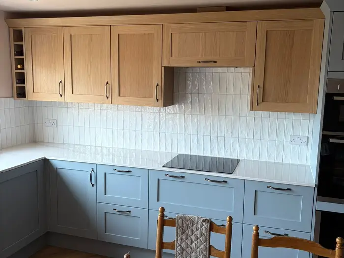 The new kitchen with oak wall units above blue-grey base units and white tiles