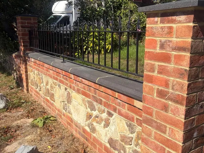 A new brick wall with flint panels, stone coping and black railings