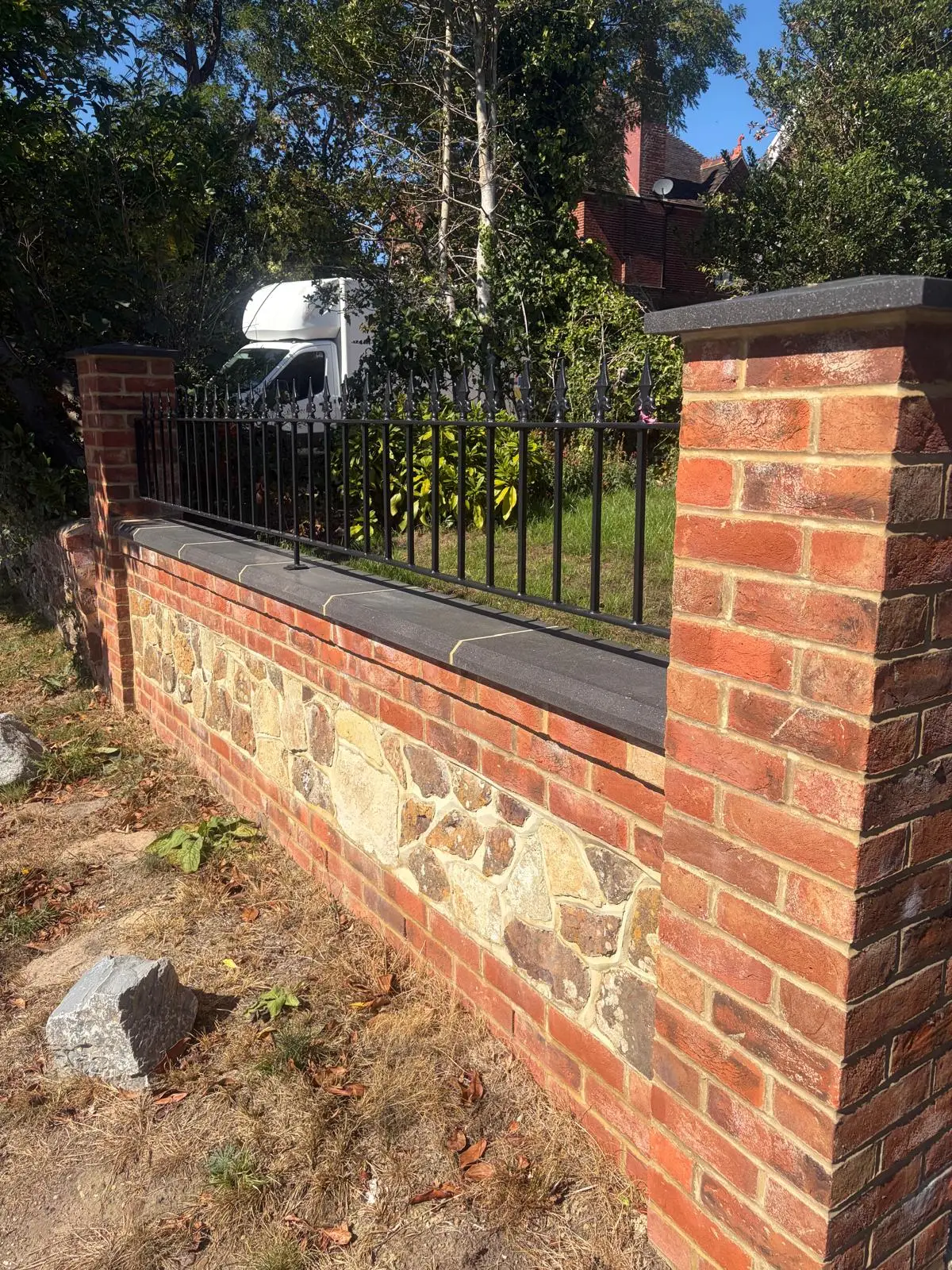The new brick wall with flint panels, dark stone coping and black railings