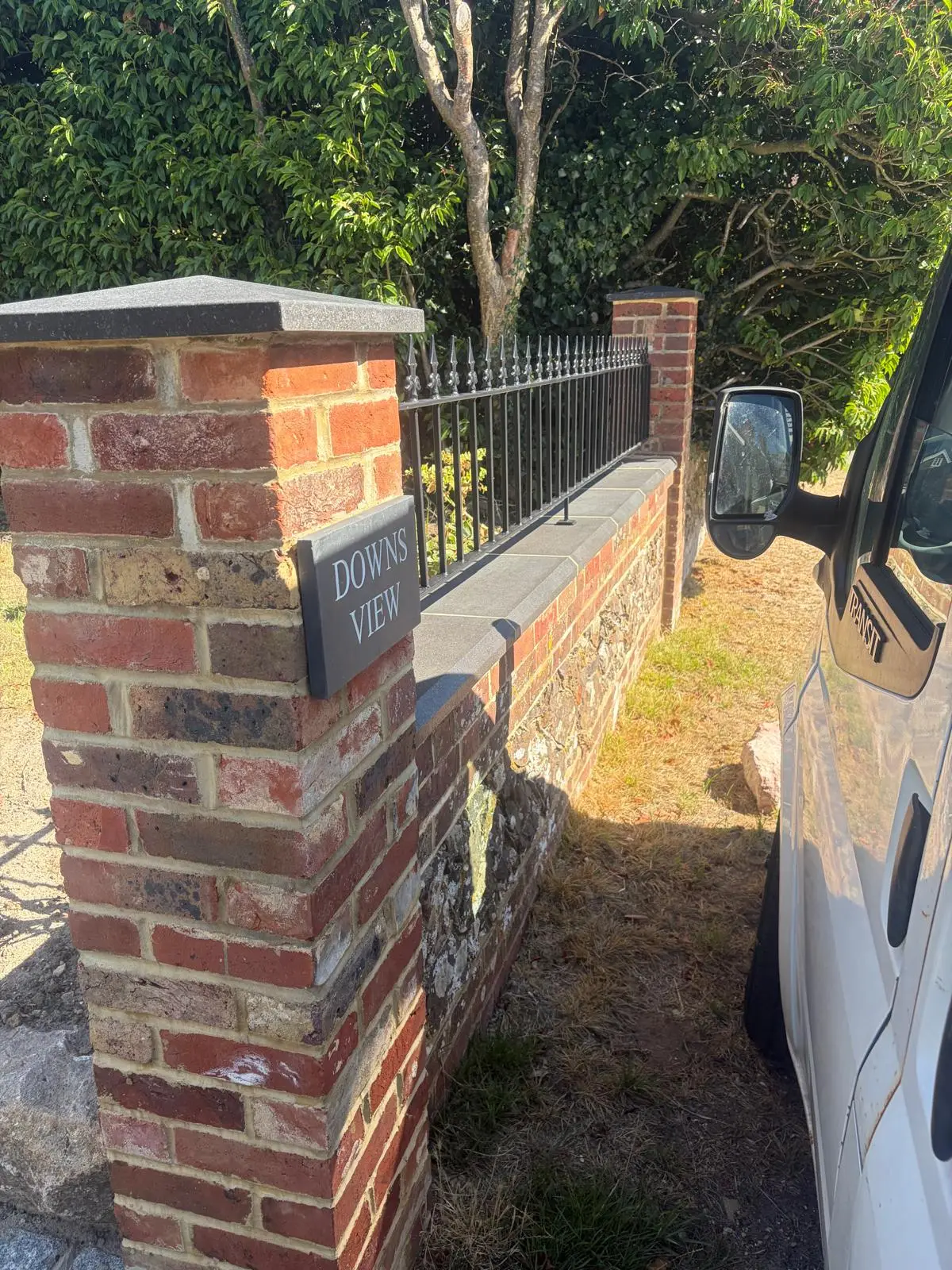 A brick pier with a stone cap and house sign at the end of the wall